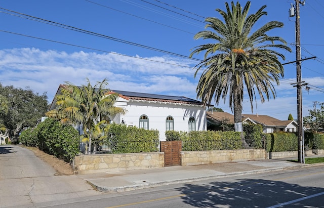 mediterranean / spanish house with a fenced front yard, solar panels, and stucco siding