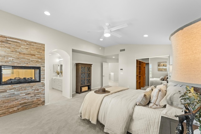 bedroom with visible vents, a multi sided fireplace, arched walkways, lofted ceiling, and light colored carpet