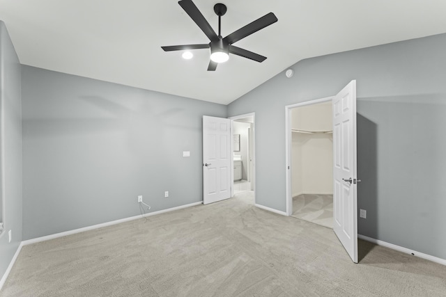 unfurnished bedroom with a walk in closet, vaulted ceiling, light colored carpet, and baseboards