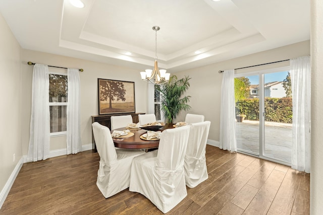 dining area featuring a raised ceiling, an inviting chandelier, and dark wood finished floors