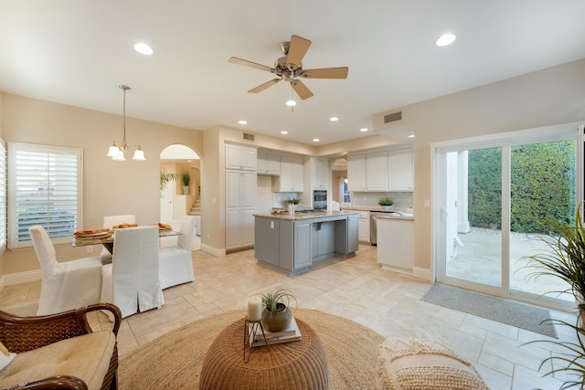 kitchen featuring visible vents, a center island with sink, light countertops, arched walkways, and white cabinetry