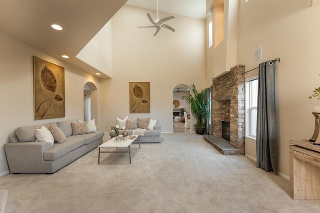 living area with visible vents, light colored carpet, a stone fireplace, recessed lighting, and arched walkways