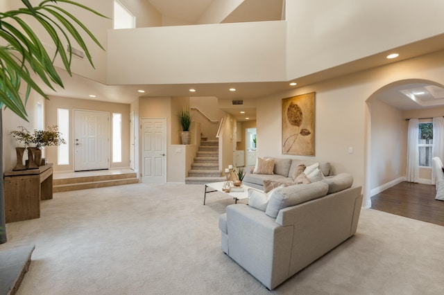 carpeted living area with recessed lighting, stairway, arched walkways, baseboards, and a towering ceiling