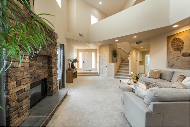 living room with a stone fireplace, visible vents, stairs, and carpet