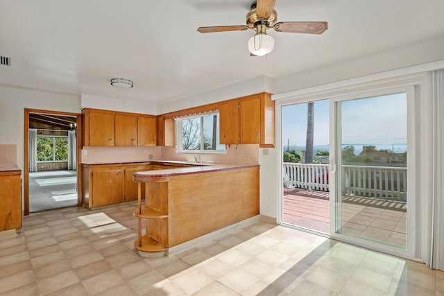 kitchen featuring visible vents, light floors, a peninsula, brown cabinetry, and open shelves