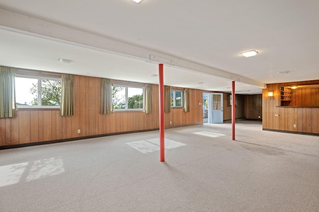 below grade area featuring light carpet, wood walls, and baseboards