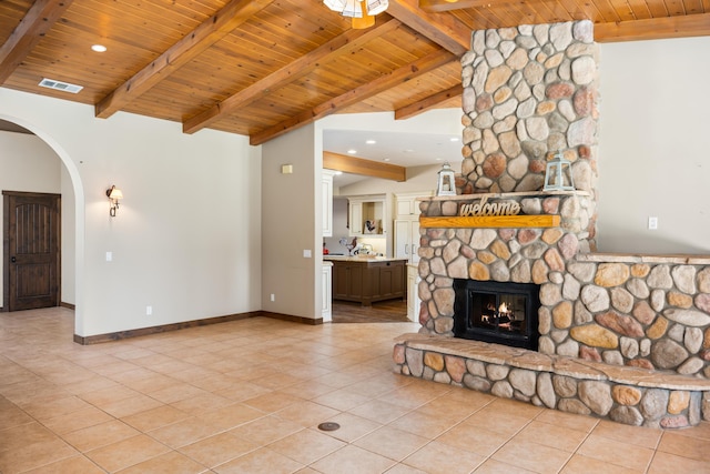 unfurnished living room with vaulted ceiling with beams, a stone fireplace, light tile patterned flooring, and visible vents