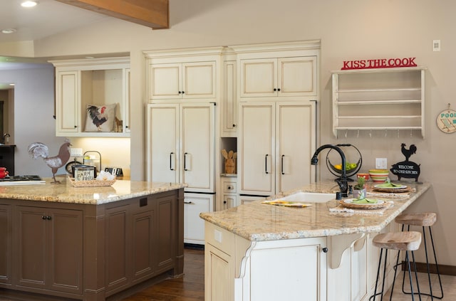 kitchen featuring light stone counters, a peninsula, a breakfast bar, cream cabinetry, and dark wood-style floors