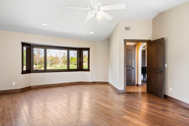 empty room featuring lofted ceiling, visible vents, baseboards, and wood finished floors