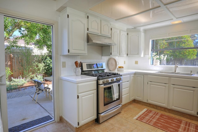 kitchen with tasteful backsplash, under cabinet range hood, light countertops, stainless steel gas stove, and a sink