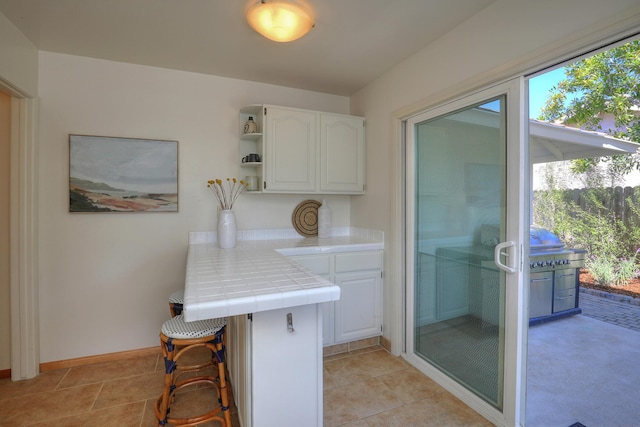 kitchen featuring tile countertops, light tile patterned floors, baseboards, open shelves, and white cabinetry