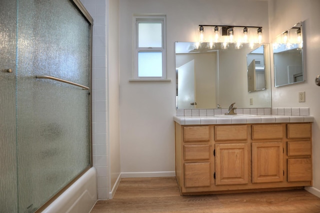 bathroom with baseboards, shower / bath combination with glass door, wood finished floors, and vanity