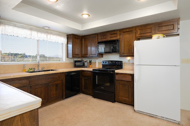 kitchen featuring tile counters, a raised ceiling, light colored carpet, black appliances, and a sink