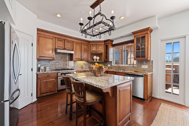 kitchen with stainless steel appliances, brown cabinets, dark wood finished floors, and under cabinet range hood