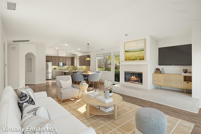 living area featuring visible vents, lofted ceiling, recessed lighting, a tile fireplace, and wood finished floors