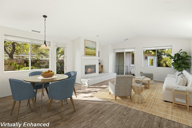 interior space featuring vaulted ceiling, a tile fireplace, visible vents, and wood finished floors