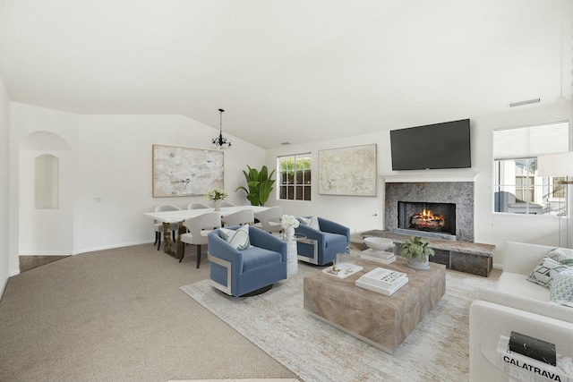 carpeted living room featuring arched walkways, visible vents, lofted ceiling, and a premium fireplace