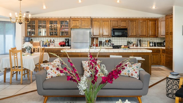 kitchen with black microwave, tile countertops, vaulted ceiling, brown cabinets, and freestanding refrigerator