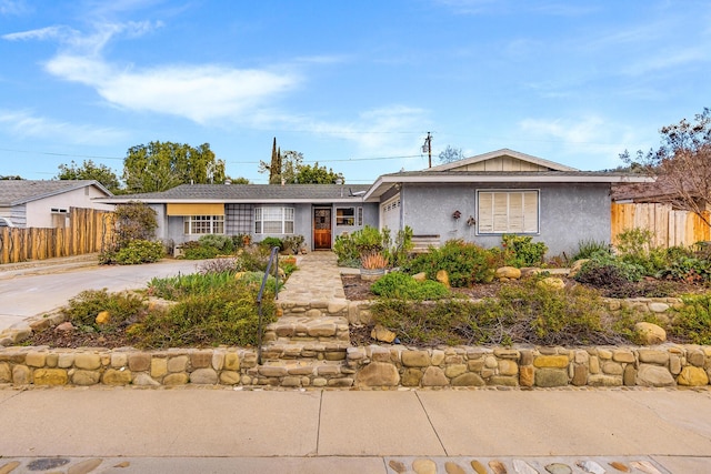 ranch-style house featuring concrete driveway, fence, and stucco siding