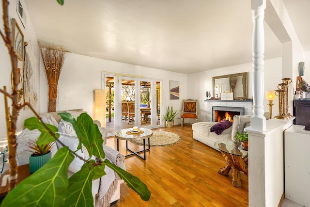 living area with visible vents, wood finished floors, french doors, decorative columns, and a brick fireplace