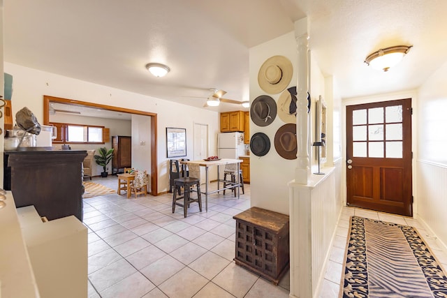 entryway with light tile patterned floors, wainscoting, a ceiling fan, and ornate columns