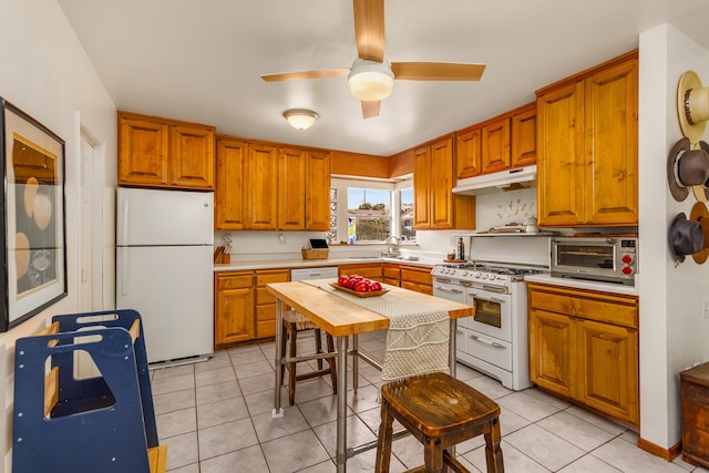 kitchen with white appliances, a toaster, light tile patterned flooring, light countertops, and under cabinet range hood