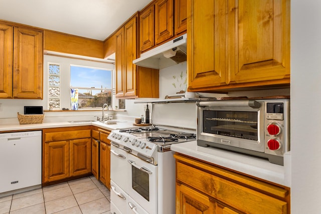 kitchen featuring white appliances, brown cabinetry, under cabinet range hood, and a sink