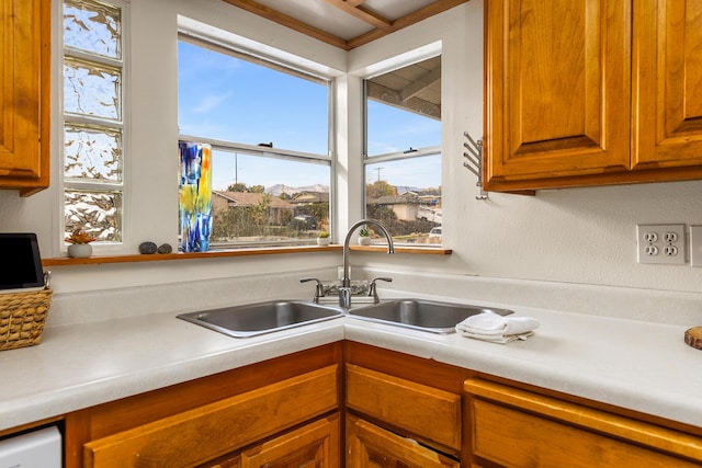 kitchen with brown cabinets, white dishwasher, light countertops, and a sink