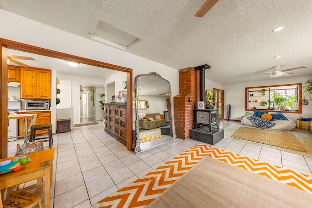 living room featuring a textured ceiling, a wood stove, light tile patterned floors, and ceiling fan