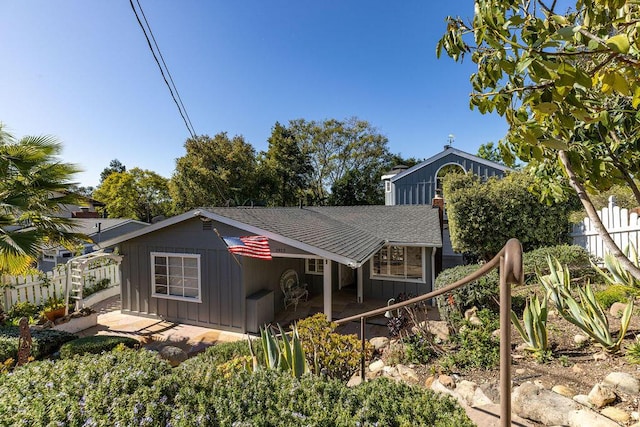 view of front facade with board and batten siding, a shingled roof, a patio, and fence