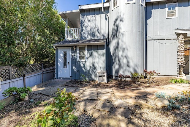 rear view of property featuring a balcony, board and batten siding, and fence