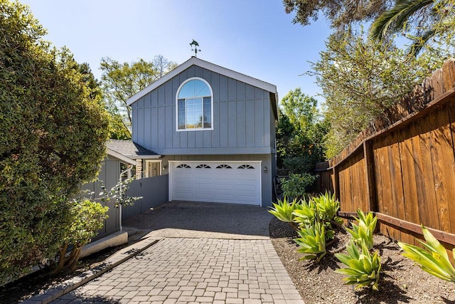 view of front facade with an attached garage, decorative driveway, and fence