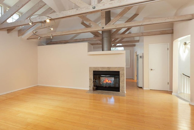 unfurnished living room with beam ceiling, high vaulted ceiling, wood finished floors, a multi sided fireplace, and baseboards