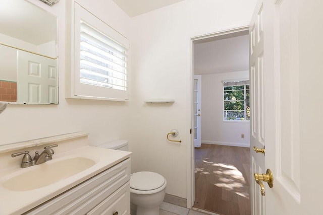 bathroom featuring baseboards, toilet, wood finished floors, and vanity