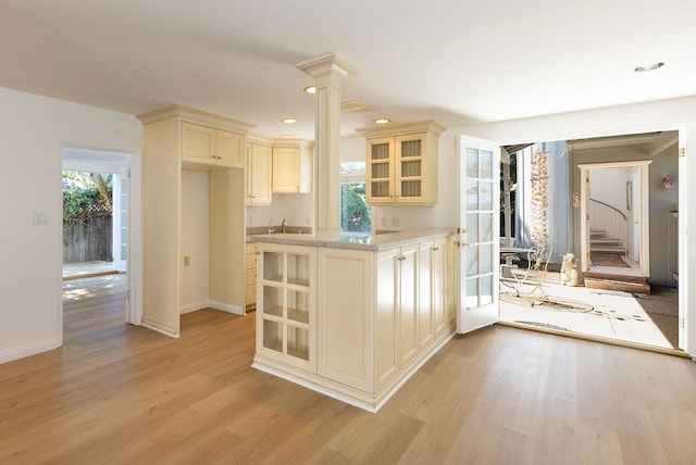 kitchen featuring glass insert cabinets, cream cabinetry, light wood-style floors, and ornate columns