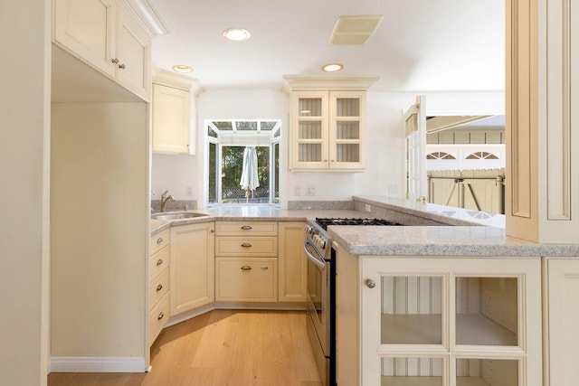 kitchen with light stone counters, light wood-style flooring, recessed lighting, a sink, and glass insert cabinets