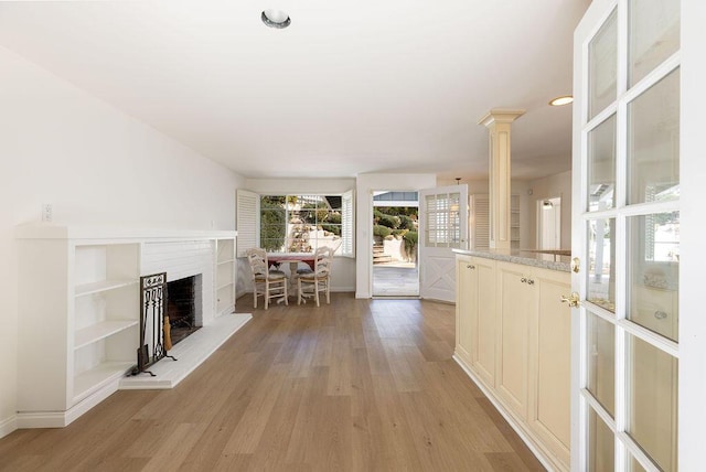 unfurnished living room with baseboards, ornate columns, light wood finished floors, recessed lighting, and a fireplace with raised hearth