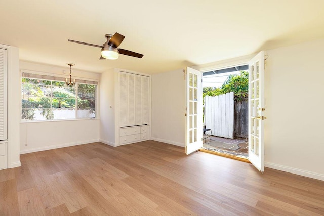 spare room with french doors, baseboards, wood finished floors, and ceiling fan with notable chandelier