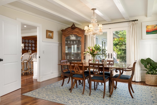 dining space with beamed ceiling, wood finished floors, wainscoting, a decorative wall, and a chandelier