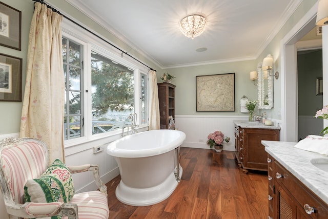 bathroom featuring wood finished floors, wainscoting, crown molding, a freestanding bath, and vanity