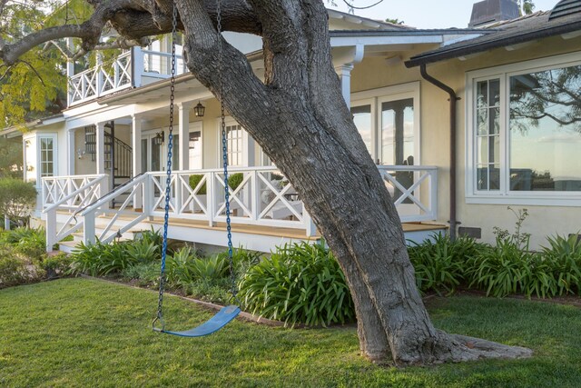 view of side of home with covered porch, stucco siding, a chimney, a lawn, and a balcony