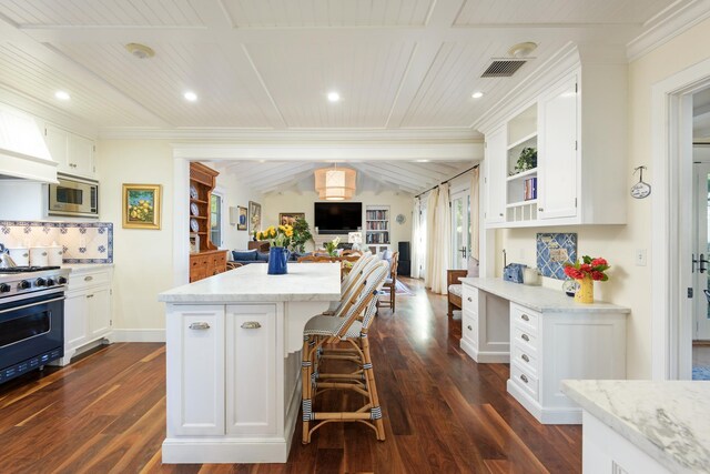 kitchen featuring a breakfast bar, stainless steel microwave, a kitchen island, gas range oven, and white cabinetry