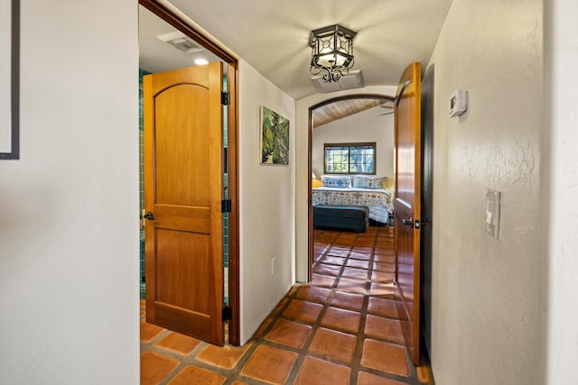 hallway with lofted ceiling, visible vents, and arched walkways