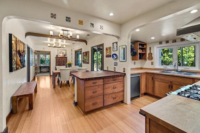 kitchen featuring a sink, stainless steel dishwasher, a peninsula, brown cabinetry, and light wood finished floors