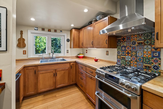 kitchen featuring brown cabinetry, double oven range, wall chimney range hood, and a sink