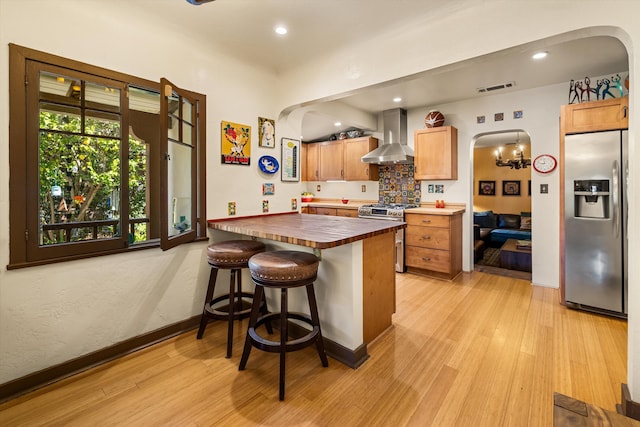 kitchen with visible vents, arched walkways, stainless steel appliances, light wood-style floors, and wall chimney exhaust hood