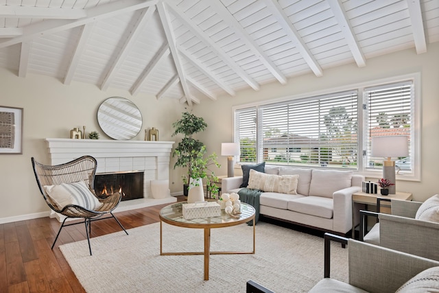 living room featuring baseboards, a brick fireplace, hardwood / wood-style floors, and vaulted ceiling with beams