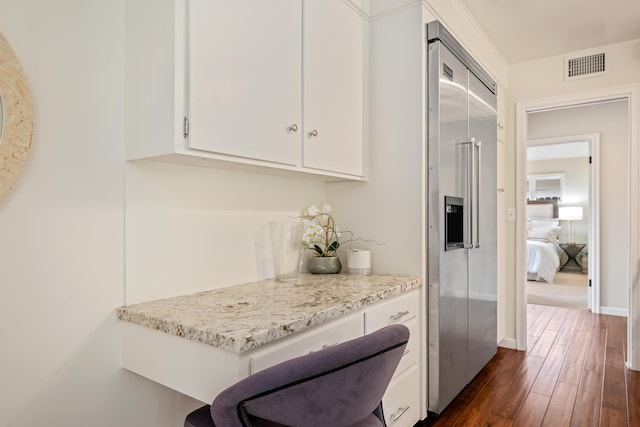 kitchen featuring light stone counters, visible vents, dark wood finished floors, white cabinets, and built in fridge