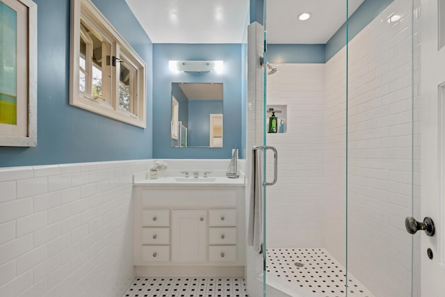 full bath with vanity, a shower stall, tile walls, and a wainscoted wall