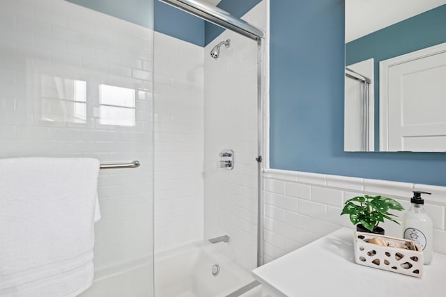 bathroom featuring tile walls, a wainscoted wall, and bath / shower combo with glass door